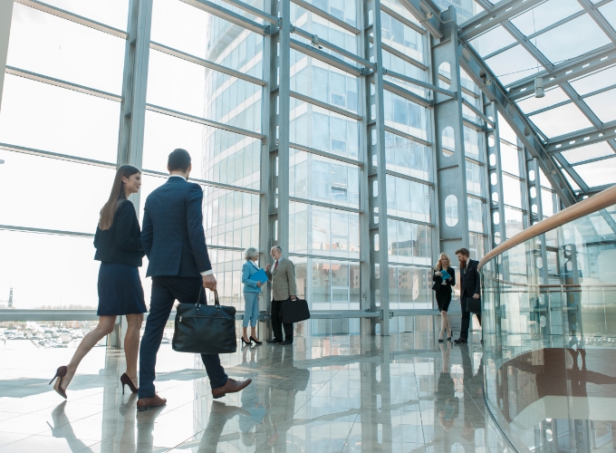 Professionals walking through a modern glass office building lobby, symbolizing healthy, sustainable, and high-performance work environments.
