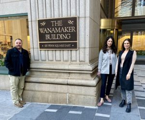 This image depicts 3 people standing outside the Wanamaker Building in Philadelphia, PA to help advertise a new office location for Hillmann Consulting, LLC