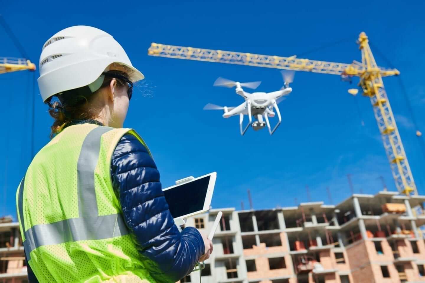 Image of a construction worker flying a drone over an active construction project.