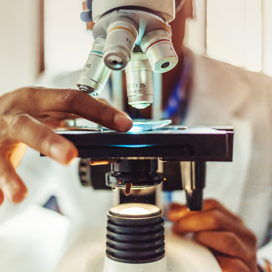 A laboratory analyst in a white lab coat examines a sample under a microscope, carefully adjusting the focus. The close-up shot highlights the precision and attention to detail required in scientific analysis.