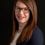 Professional headshot of Kristen Brink, PE, Principal/Partner at Hillmann Consulting, wearing glasses and a navy blazer against a dark background.